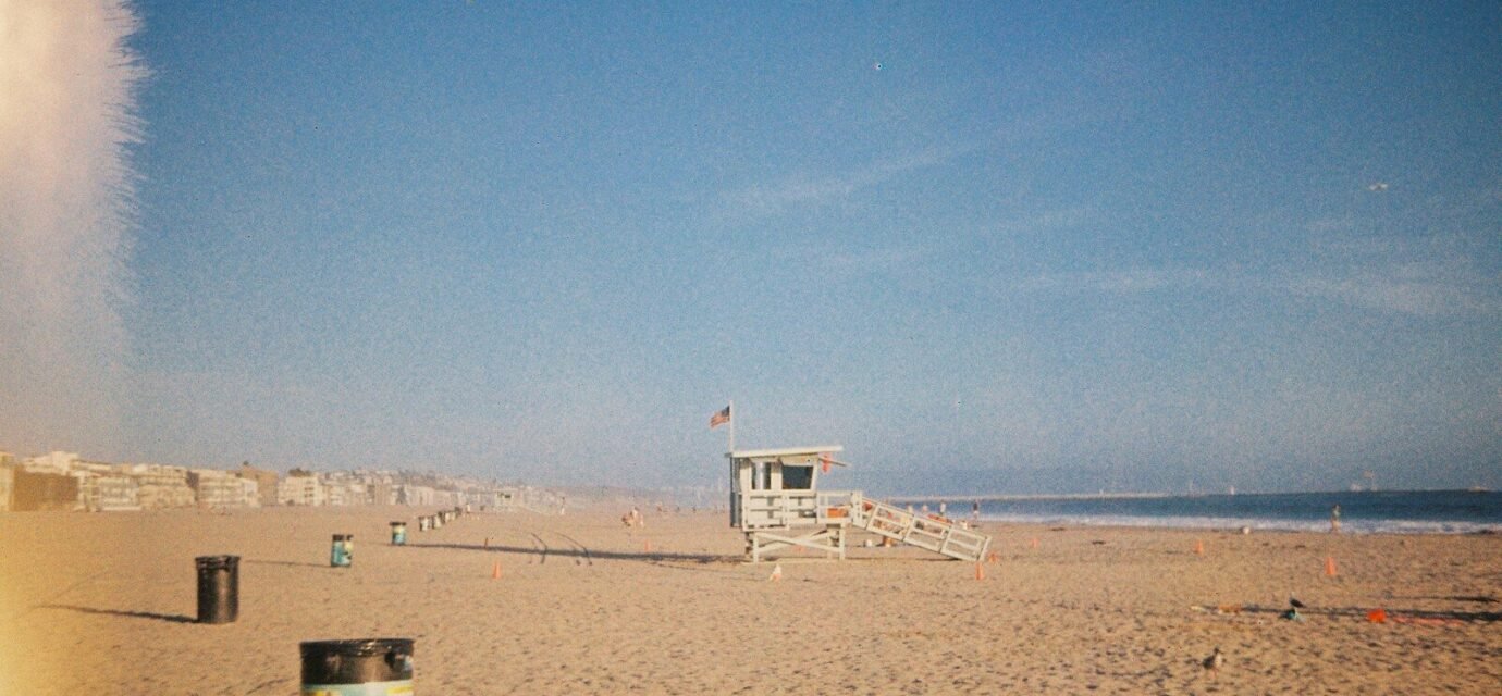 A wooden lifeguard tower on a sandy beach under a clear blue sky.