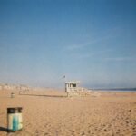 A wooden lifeguard tower on a sandy beach under a clear blue sky.
